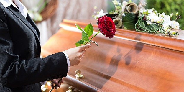 Mourning woman on funeral with red rose standing at casket or coffin